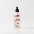 Bottle of Rose Body Oil with rose petals suspended inside and a black pump dispenser on a white background